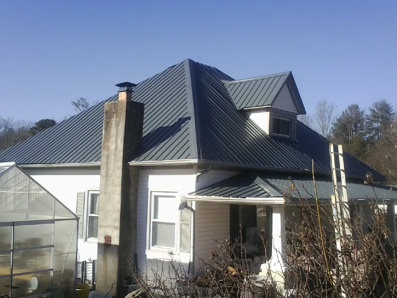 Dark blue standing seam metal roof on a white farmhouse with dormer — Slate & Tile Roof Repair by Roofing Brothers in Glenford