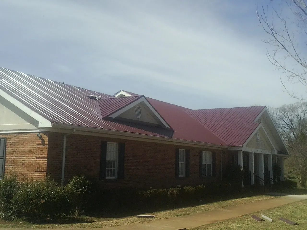 Red metal roof with gabled entries on a long brick building, from a Hail Damage Roof Repair job in Glenford