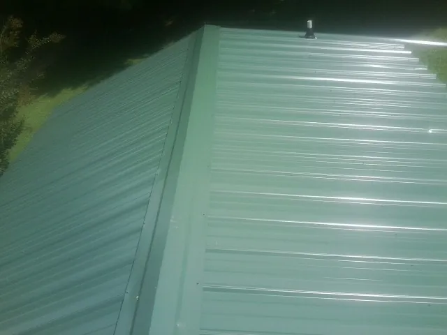 New green metal panels meeting at the ridge of a roof — Flat Roof Repair work by our crew in Glenford