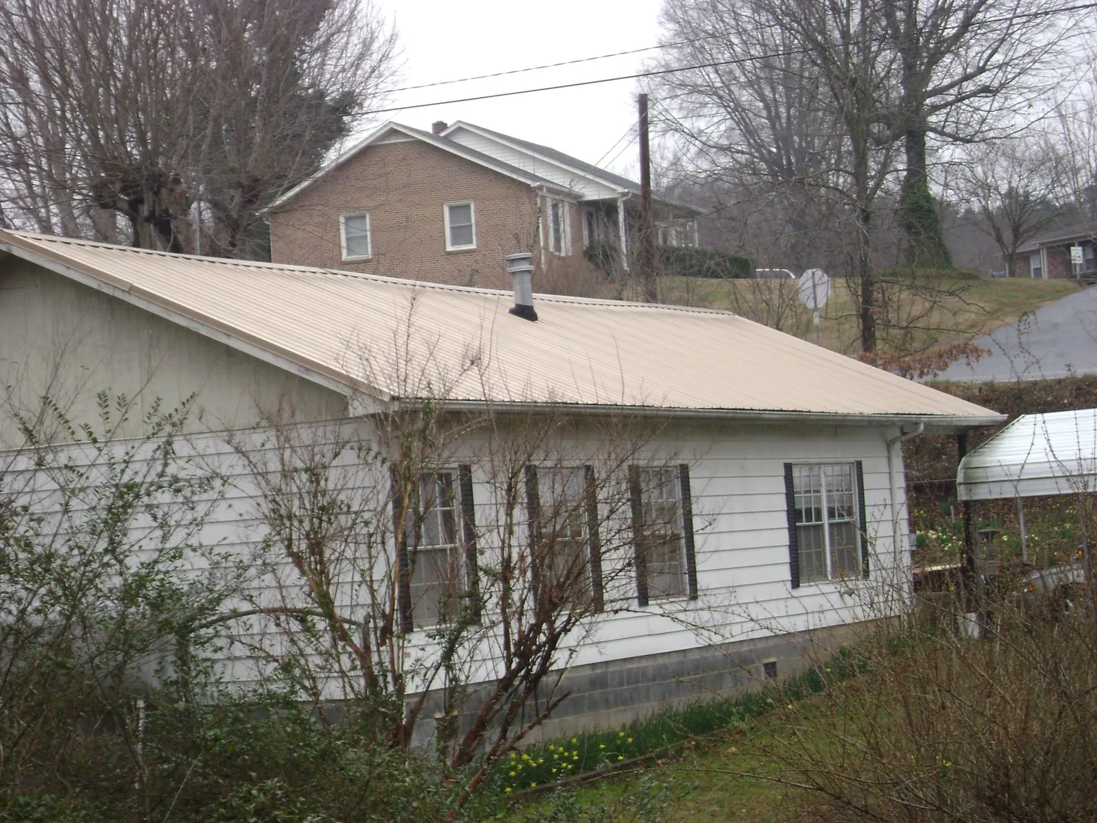 Tan metal roof on a white sided house set into a hillside — Commercial Roofing by Roofing Brothers in Glenford
